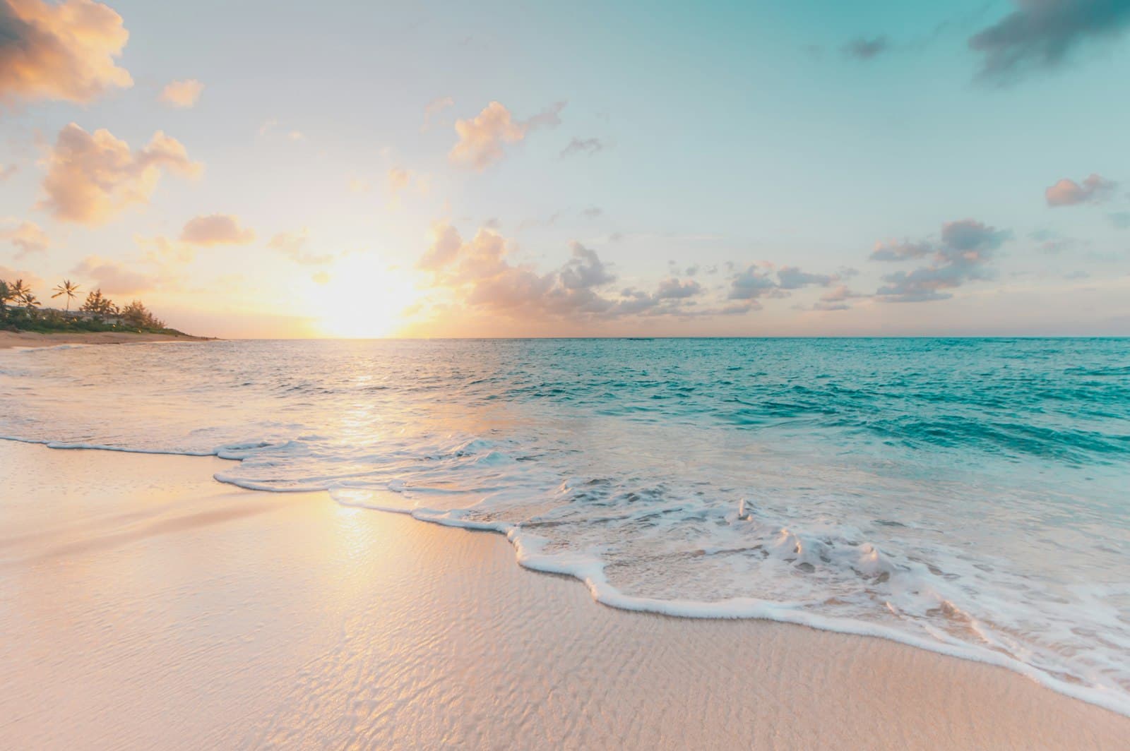 A tropical beach at sunset with calm waves rolling onto golden sand
